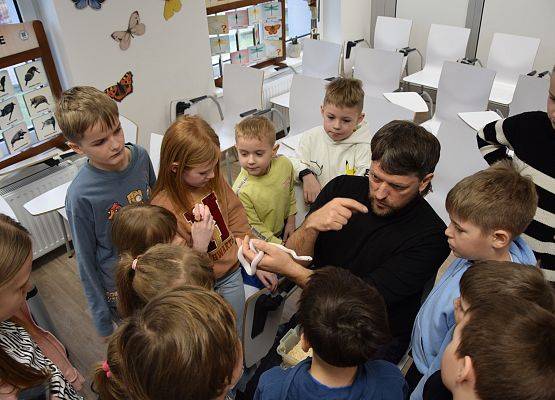 Grupa dzieci zgromadzona wokół edukatora trzymającego małego węża.