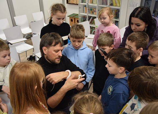 Grupa dzieci zgromadzona wokół edukatora trzymającego małego węża.