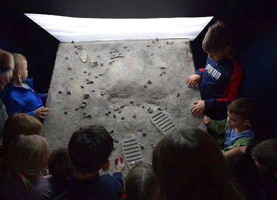 Grupa dzieci zgromadzona wokół makiety Księżyca w sali astronomicznej Zielonej Szkoły