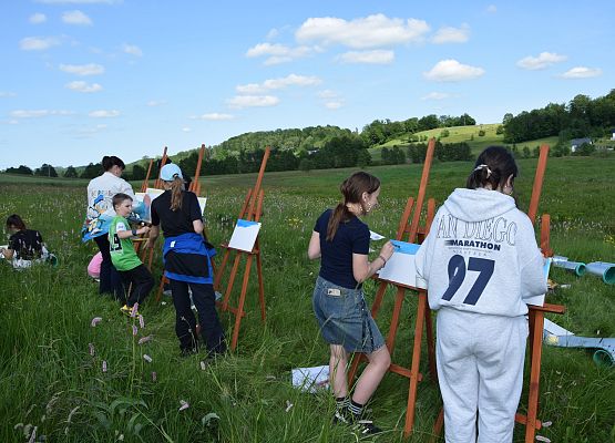 Uczestnicy wyposażeni w sztalugi i podobrazia malują łąkę