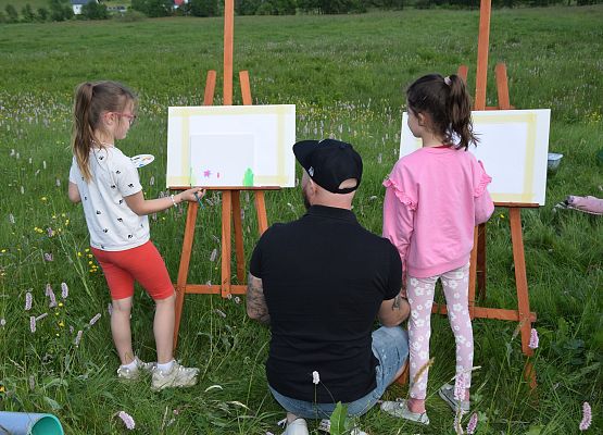 Dwójka dzieci pod okiem opiekuna maluje obrazy na malowniczej łące
