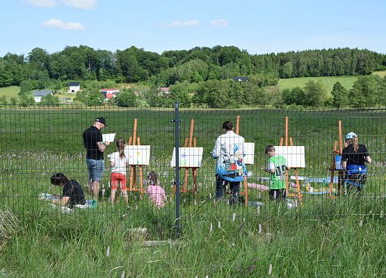 Uczestnicy warsztatów stoją przy sztalugach i malują łąkę